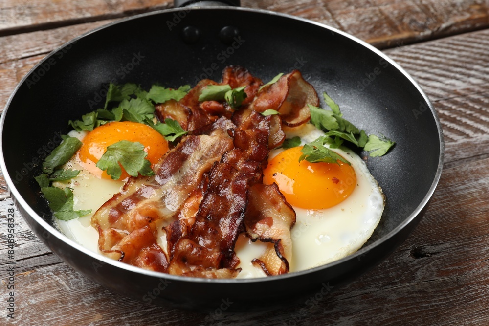 Tasty bacon, eggs and parsley in frying pan on wooden table, closeup Tasty bacon, eggs and parsley in frying pan on wooden table, closeup
