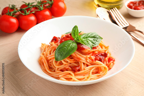 Delicious pasta with tomato sauce and basil in bowl on wooden table, closeup