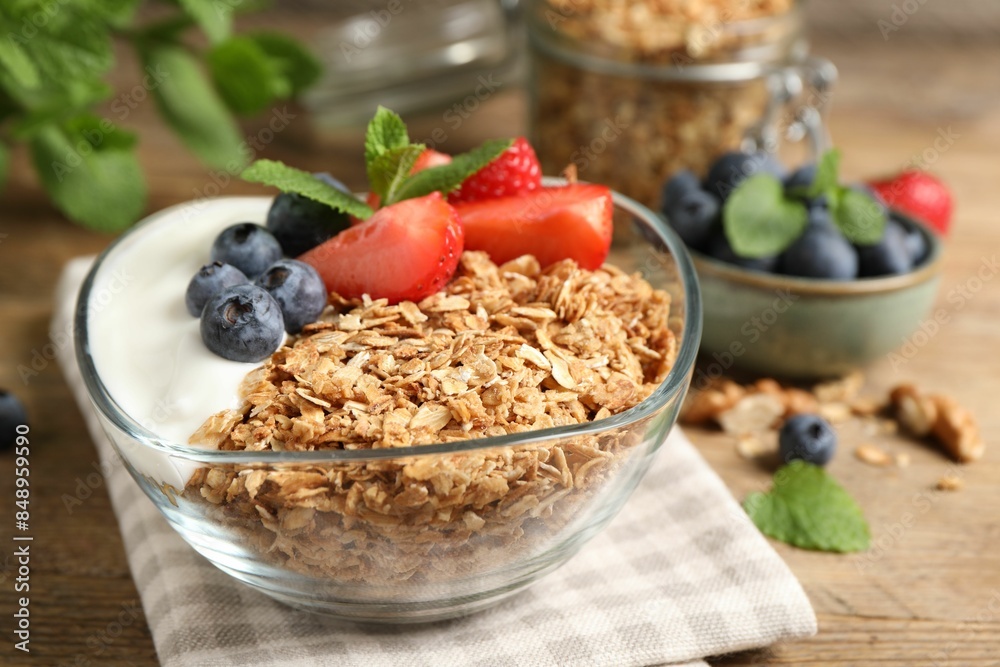 Tasty granola with berries and yogurt in bowl on wooden table, closeup