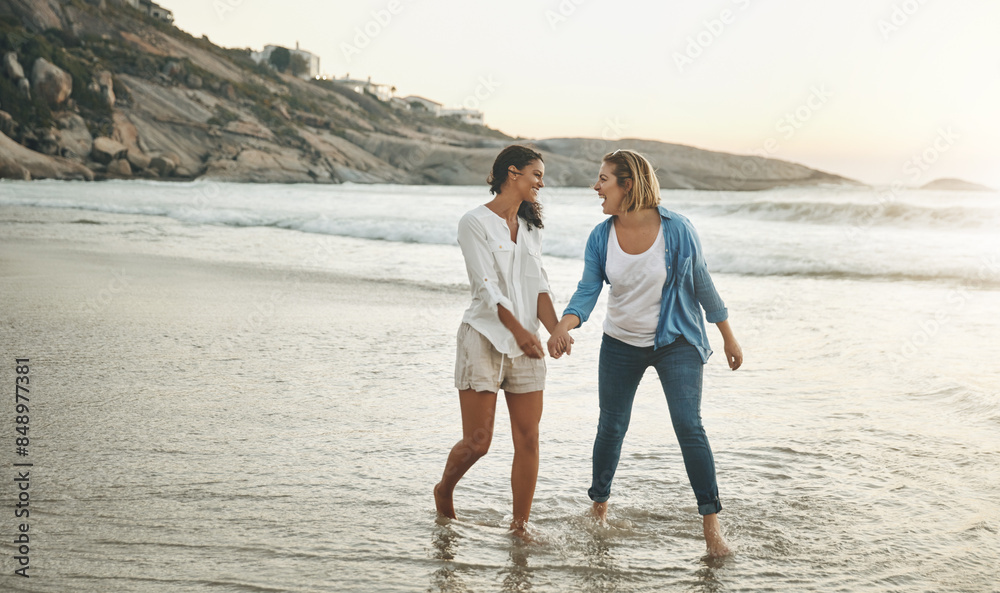 Fototapeta premium Holding hands, couple and water in beach, lesbian and women on sand, vacation and walking with love. Summer, travel and waves in sea, holiday and peace of people, lgbtq and trust in adventure of date
