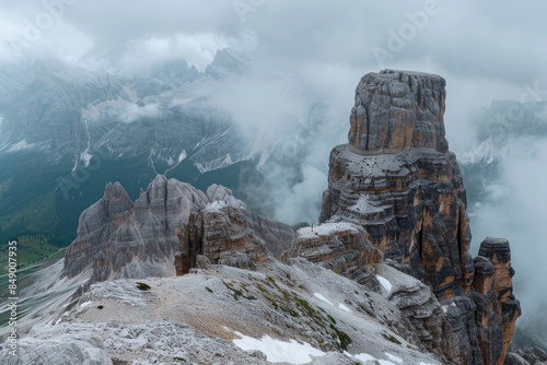 Photo of Mt Jelly in the Dolomites, Italy. The peak is isolated and surrounded by rugged mountains with some snow patches. It's an overcast day with low clouds.