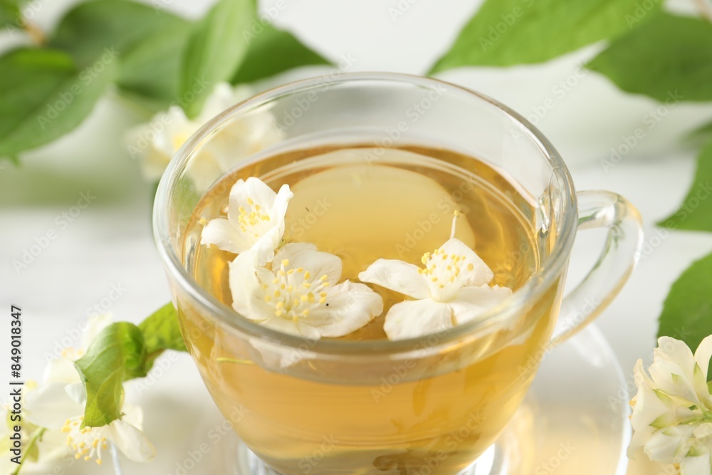 Aromatic jasmine tea in cup, flowers and green leaves on table, closeup Aromatic jasmine tea in cup, flowers and green leaves on table, closeup