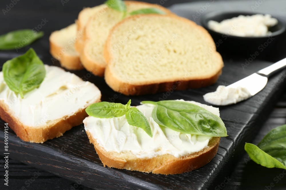 Pieces of bread with cream cheese and basil leaves on black table, closeup Pieces of bread with cream cheese and basil leaves on black table, closeup