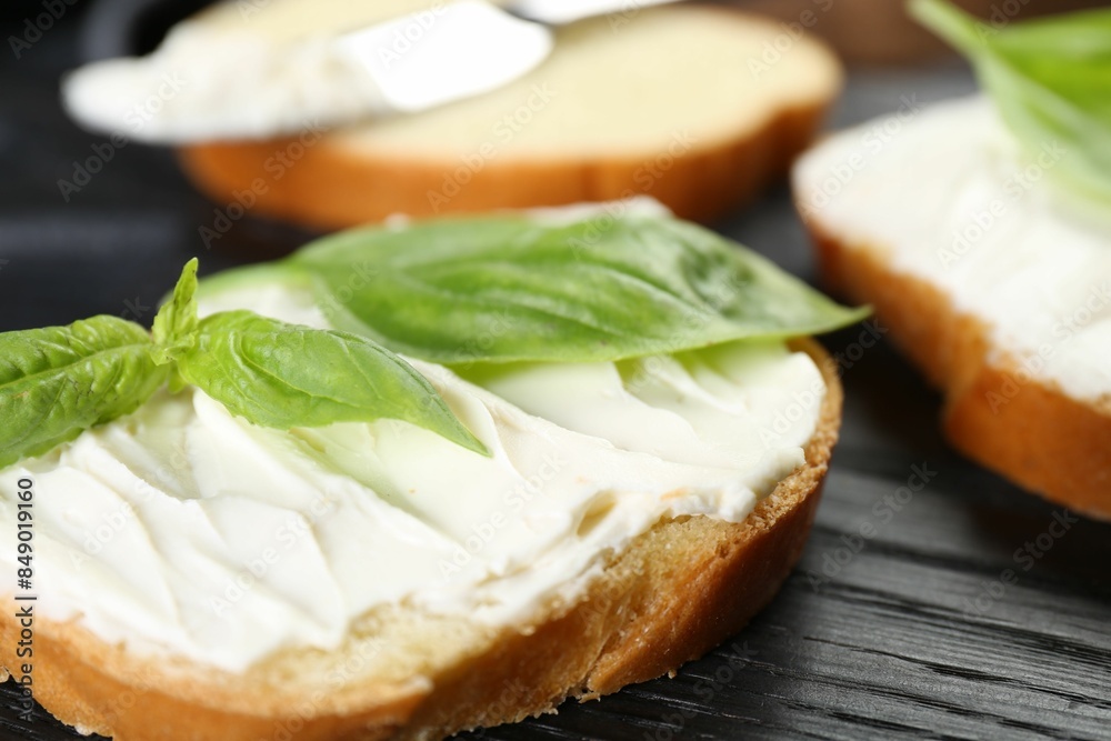 Piece of bread with cream cheese and basil on black wooden table, closeup Piece of bread with cream cheese and basil on black wooden table, closeup