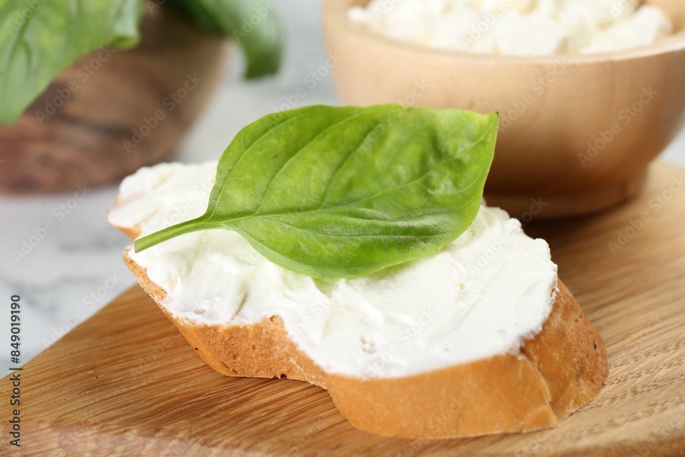 Piece of bread with cream cheese and basil leaf on white table, closeup Piece of bread with cream cheese and basil leaf on white table, closeup