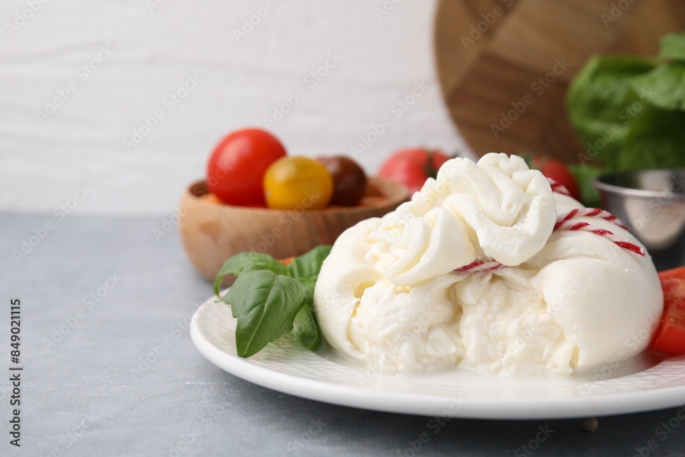 Delicious fresh burrata cheese with basil leaves on grey table, space for text Delicious fresh burrata cheese with basil leaves on grey table, space for text