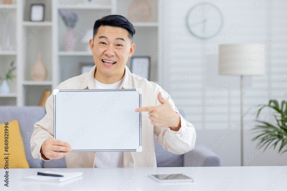 Happy man smiling and pointing at a blank whiteboard in a modern home office environment. Great for messaging, presentations, and promotional content. Happy man smiling and pointing at a blank whiteboard in a modern home office environment. Great for messaging, presentations, and promotional content.