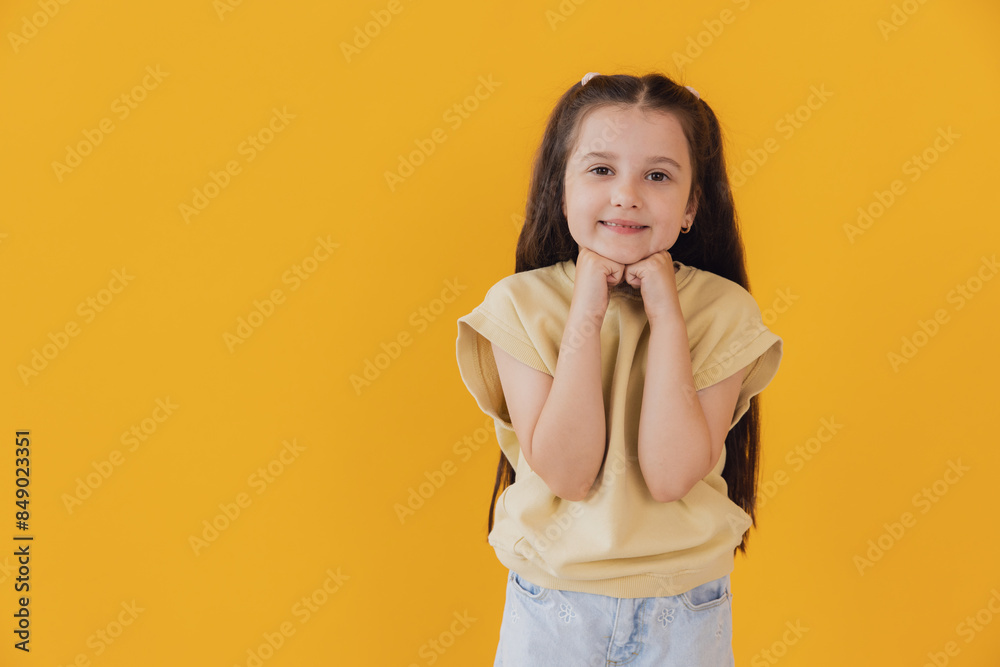 A wonderful little girl with folded hands near her face smiling on a yellow background A wonderful little girl with folded hands near her face smiling on a yellow background