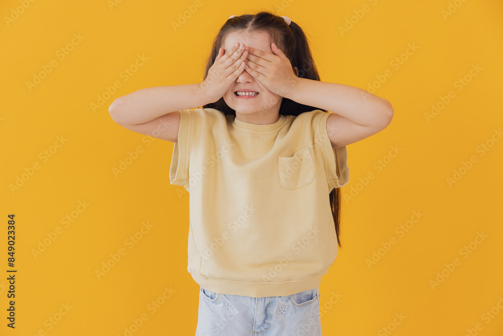 Portrait of smiling girl child kid cover eyes with hands isolated on yellow color background