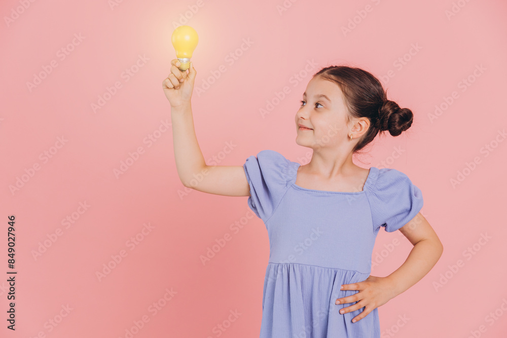 Cute smiling little girl holding glowing light bulb on pink background with copy space Cute smiling little girl holding glowing light bulb on pink background with copy space
