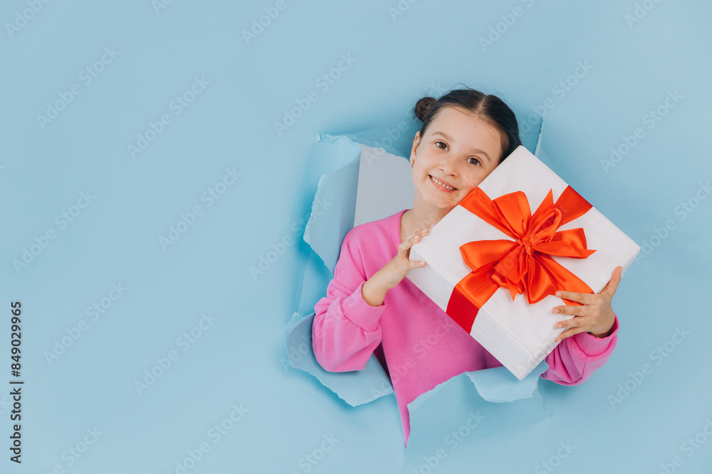 Adorable little girl peeking from ripped paper hole and holding gift. Valentines, Mother day, birthday or celebration concept. Adorable little girl peeking from ripped paper hole and holding gift. Valentines, Mother day, birthday or celebration concept.