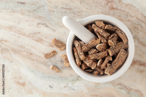 Top-view of Dry Organic Sweet flag or Vach (Acorus calamus) roots, in white ceramic mortar and pestle, on a marble background.