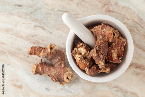 Top-view of Dry Organic Kulanjan (Alpinia galanga) roots, in white ceramic mortar and pestle, on a marble background. photo