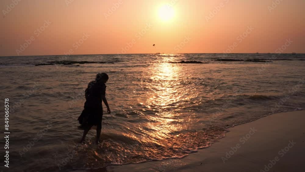 Young Indian woman walking on the Goa beach against the setting sun background. Indian female tourist walks along the beach at sunset. Young Indian woman walking on the Goa beach against the setting sun background. Indian female tourist walks along the beach at sunset.