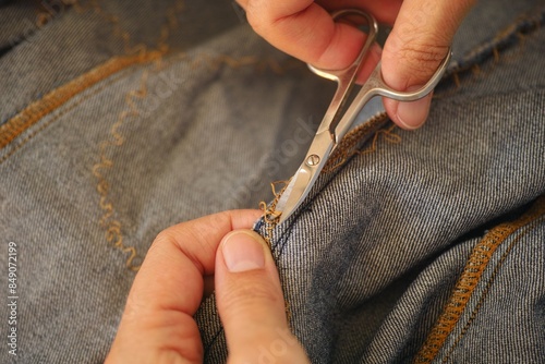 A woman hands with scissors cutting open the seam on a  jeans dress