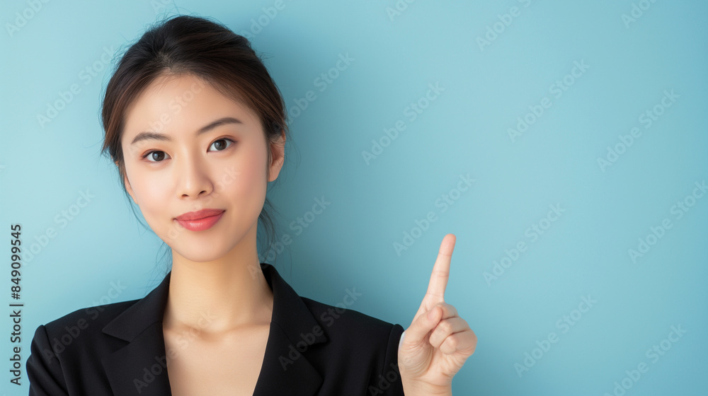 A confident Asian woman presenting with a pointing gesture, her elegance highlighted against a clean light blue backdrop. A confident Asian woman presenting with a pointing gesture, her elegance highlighted against a clean light blue backdrop.