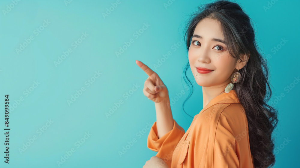 Fototapeta premium A beautiful young Asian woman elegantly pointing to a copy space light blue background, capturing her confidence and grace.