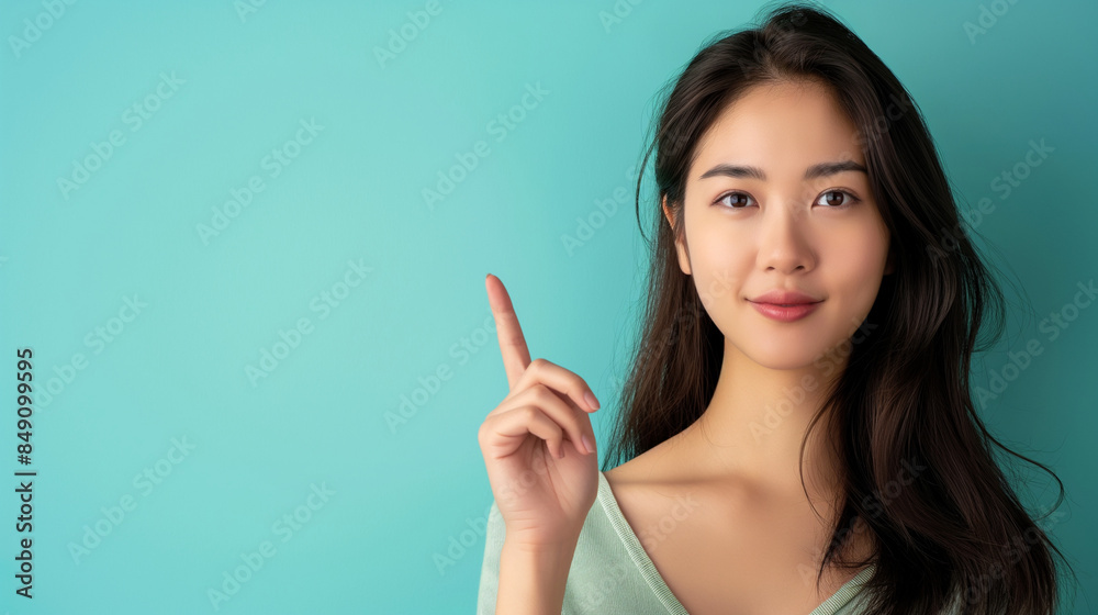 A beautiful young Asian woman elegantly pointing to a copy space light blue background, capturing her confidence and grace. A beautiful young Asian woman elegantly pointing to a copy space light blue background, capturing her confidence and grace.
