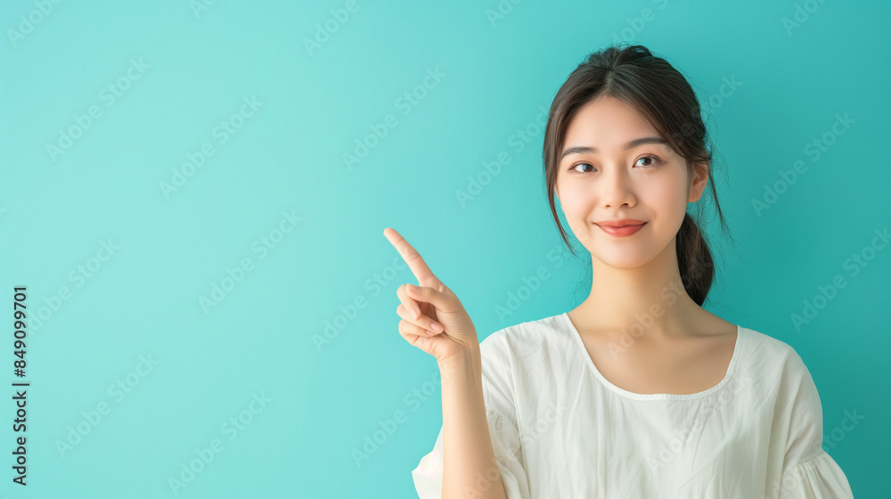 An elegant Asian woman presenting with confidence, pointing towards a light blue background with ample copy space. An elegant Asian woman presenting with confidence, pointing towards a light blue background with ample copy space.