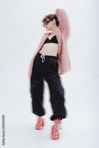 Full length photo of amazing model in photo studio, stylish pink fur coat, sweatpants, sunglasses, high heels. Fashion, style