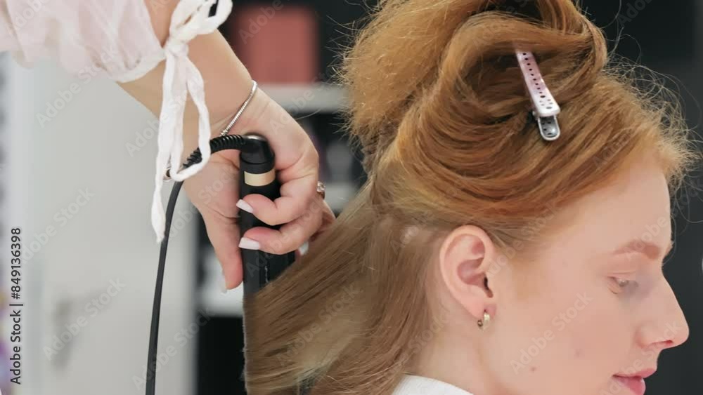 A hairstylist uses a curling iron to style a woman's hair in a salon. The detailed process of hair styling, emphasizing personal care and professional beauty services. A hairstylist uses a curling iron to style a woman's hair in a salon. The detailed process of hair styling, emphasizing personal care and professional beauty services.