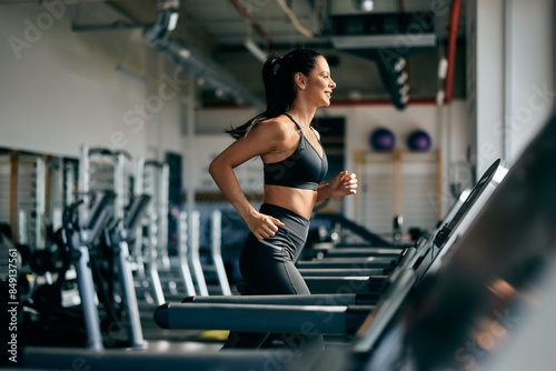 Foto Side profile of a smiling fit woman running on a treadmill at the gym