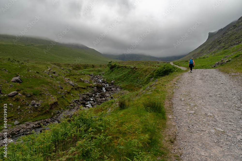 Fototapeta premium Hiker girl on Devils Ladder, one of most difficult trails, that is leading to highest Irish mountain Carrauntoohill or Carrantuohill is the highest mountain in Ireland at 1038m