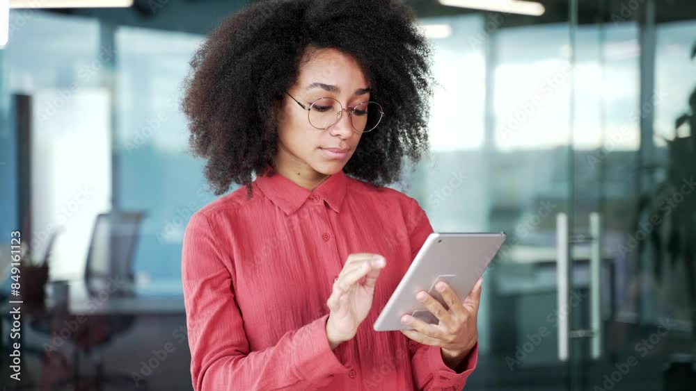Confident young african american female employee is using digital tablet standing in business office. Focused Black woman works on application, reading typing message, browsing web or chatting online Confident young african american female employee is using digital tablet standing in business office. Focused Black woman works on application, reading typing message, browsing web or chatting online