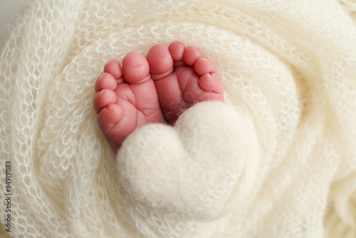 The tiny foot of a newborn baby. Soft feet of a new born in a white wool blanket. Close up of toes, heels and feet of a newborn. Knitted white heart in the legs of a baby. Macro photography © Vad-Len