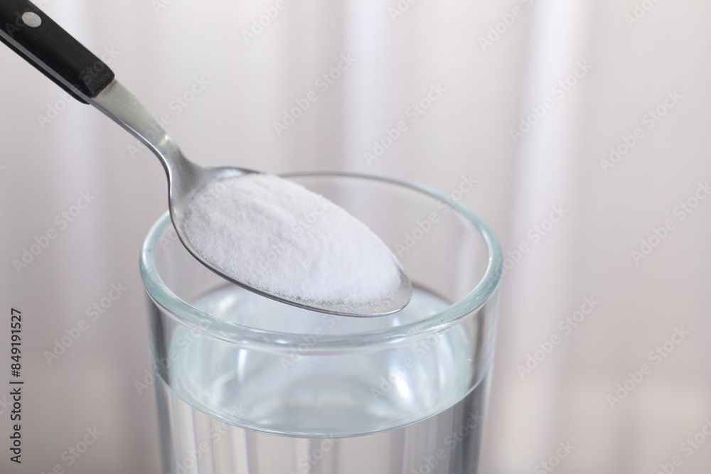 Adding baking soda into glass of water on light background, closeup Adding baking soda into glass of water on light background, closeup