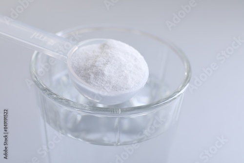 Spoon with baking soda over glass of water on light grey background, closeup