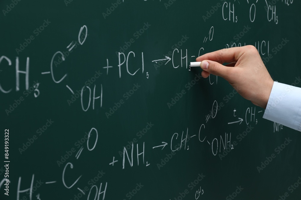 Teacher writing chemical formulas with chalk on green chalkboard, closeup Teacher writing chemical formulas with chalk on green chalkboard, closeup