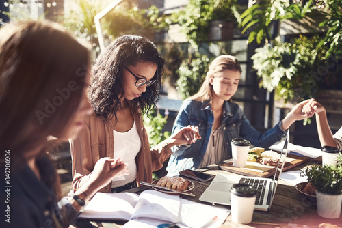 Women, restaurant and holding hands for prayer or grace to bless food and lunch. Colleagues, unity and care with thanks, appreciation and grateful for meal with laptop or paperwork for teambuilding