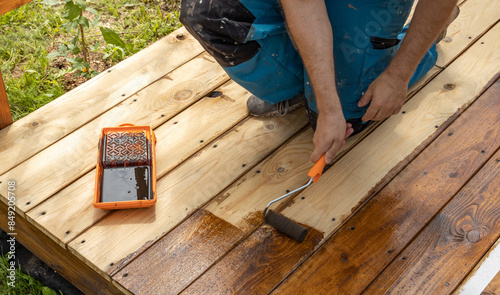 Wallpaper Mural A person in blue overalls applies a dark stain to a wooden deck using a paint roller. Torontodigital.ca