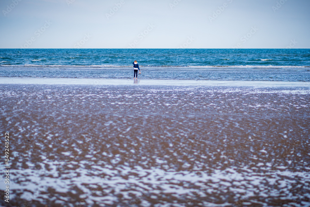 Sporty woman with sneakers in her hand on the sandy beach during windy day. Back view. Low angle. Donabate beach, Ireland Sporty woman with sneakers in her hand on the sandy beach during windy day. Back view. Low angle. Donabate beach, Ireland