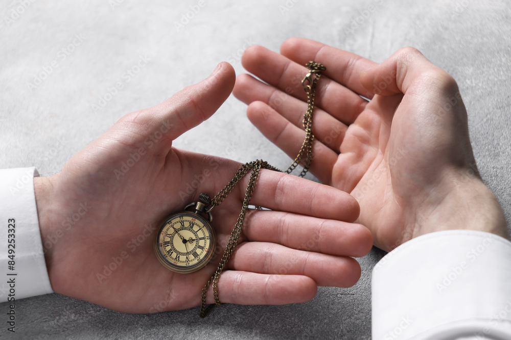 Fototapeta premium Man holding chain with elegant pocket watch at grey textured table, closeup