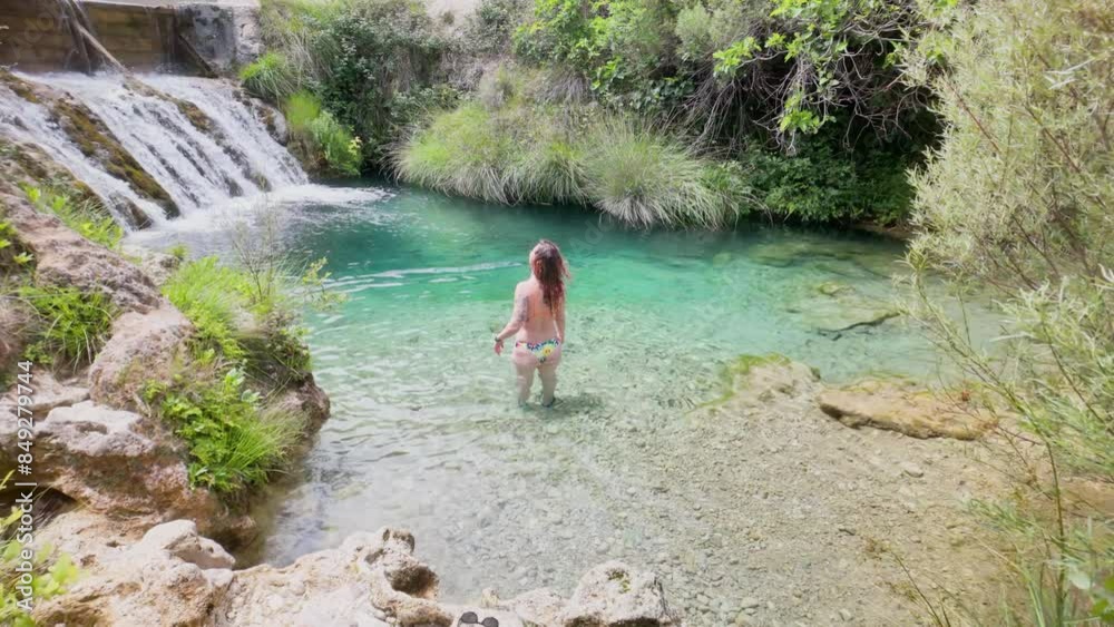 A woman is walking in a stream. The water is clear and the surrounding area is lush and green A woman is walking in a stream. The water is clear and the surrounding area is lush and green