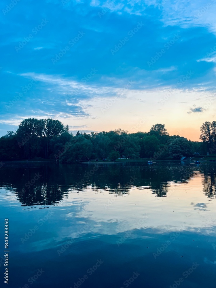 Fototapeta premium Fantastic cloudy sky reflection on the lake surface, trees silhouettes reflection on the lake, evening twilights lake in the park