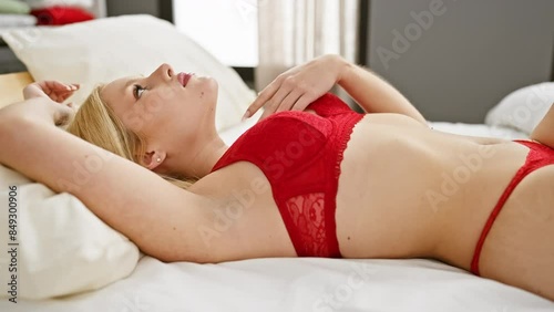 Young blonde woman in red lingerie lying on bed, indoor bedroom setting, sensuality, comfort, and allure