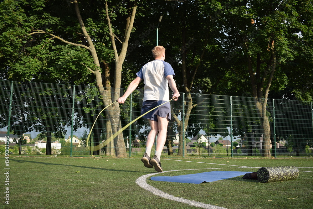 Obraz premium A young man in sportswear engages in a workout, using a sport tool for physical exercises on a sports field in the morning. His dedication to fitness performs training routine with focus and energy