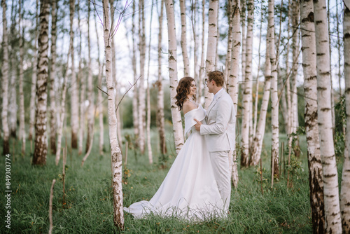 Canvas Print Valmiera, Latvia - September 9, 2023 - Bride and groom stand in a birch forest, gazing lovingly at each other amidst tall trees and lush green grass on their wedding day
