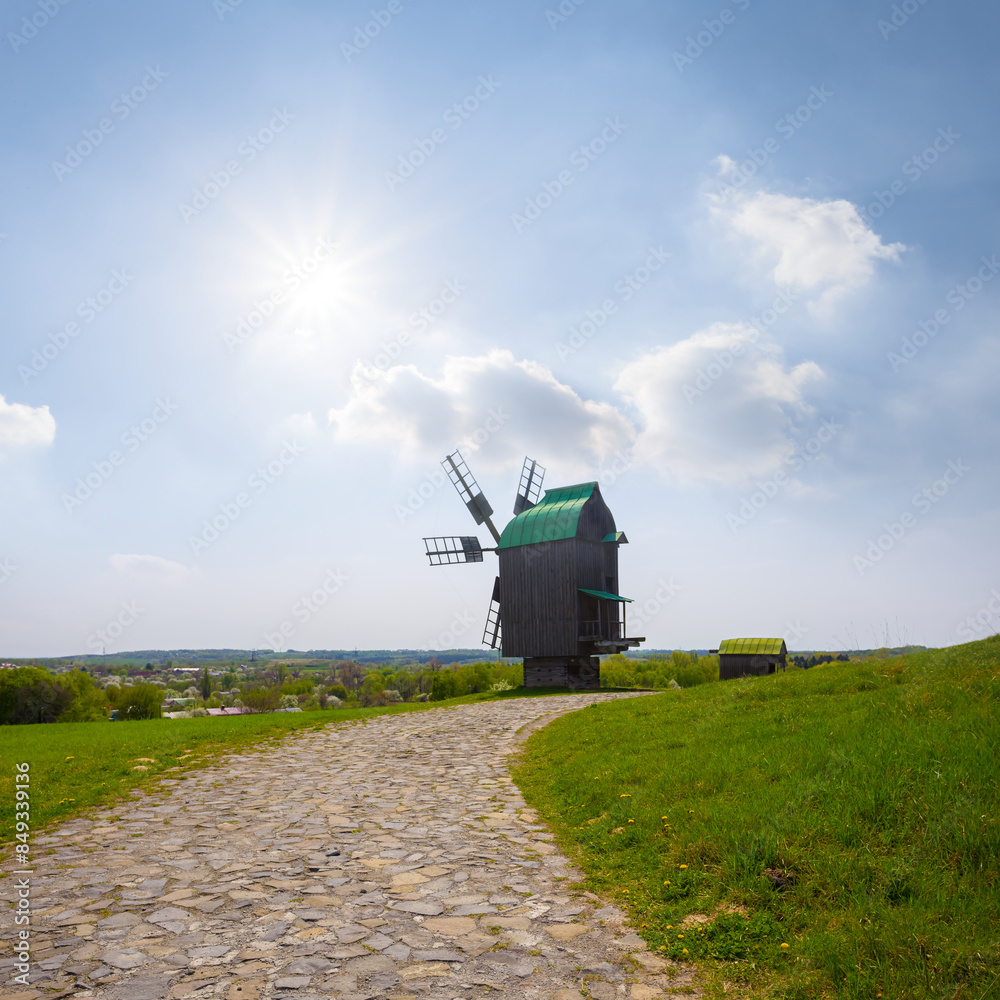Fototapeta premium old wooden medieval windmill among green rural fields at summer sunny day