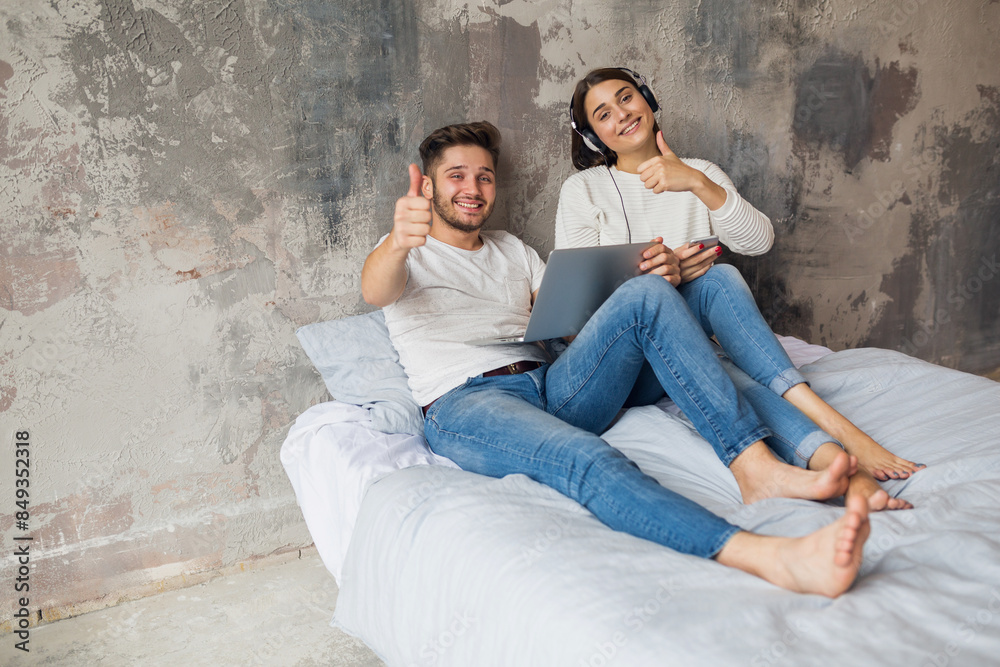 young happy smiling couple sitting on bed at home young happy smiling couple sitting on bed at home