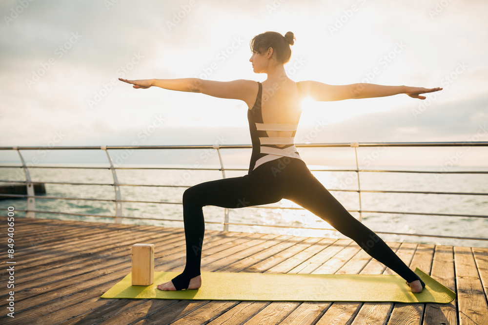 Fototapeta premium young slim beautiful attractive woman doing yoga in the morning on sunrise by sea