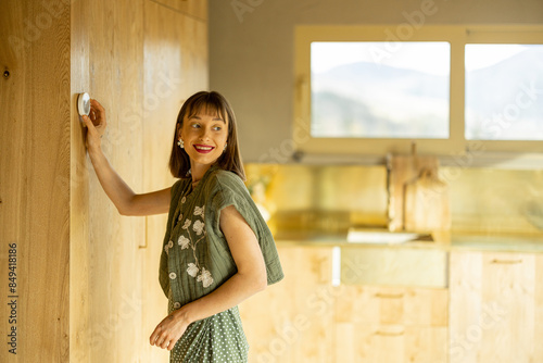 Young woman controls home temperature with smart controller thermostat at home. Concept of smart home technologies for comfort living photo