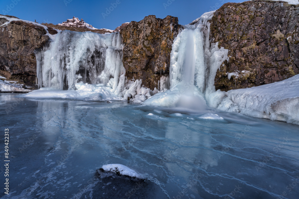 Frozen Kirkjufellfoss or Kirkjufell waterfall during a beautiful sunrise covered in snow and ice in Iceland Frozen Kirkjufellfoss or Kirkjufell waterfall during a beautiful sunrise covered in snow and ice in Iceland
