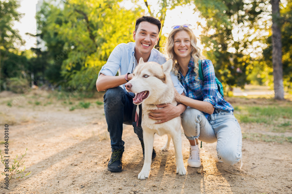 funny young stylish couple playing with dog in park