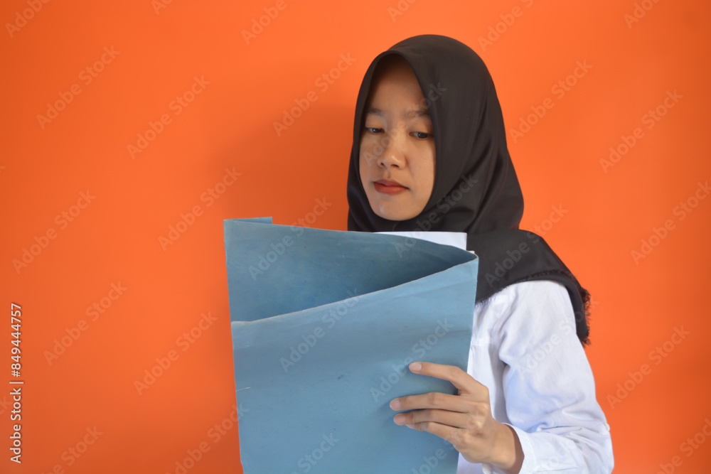 An Asian Muslim woman wearing formal white clothes and a black hijab is carrying a job application form An Asian Muslim woman wearing formal white clothes and a black hijab is carrying a job application form