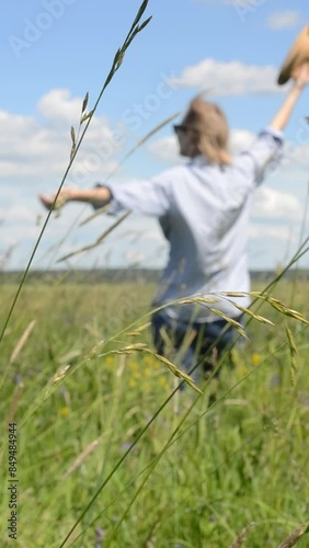 Happy woman having fun in a green field wearing a hat and blue shirt. Summer mood. Vertical video footage. 