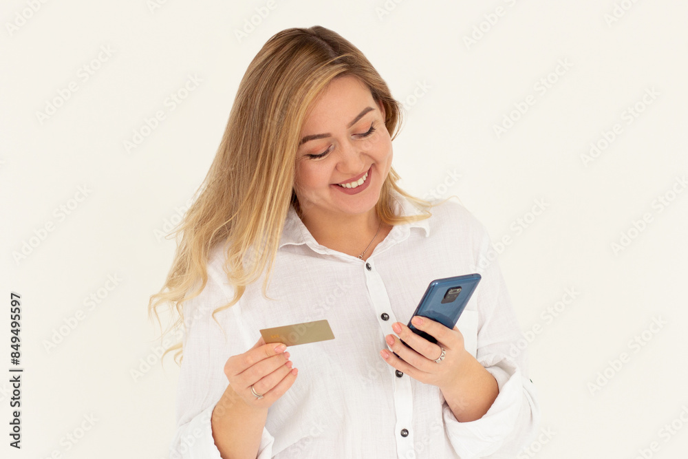 Online shopping. Smiling good-looking woman paying for order, using plastic credit card to pay with mobile phone, standing against white background Online shopping. Smiling good-looking woman paying for order, using plastic credit card to pay with mobile phone, standing against white background
